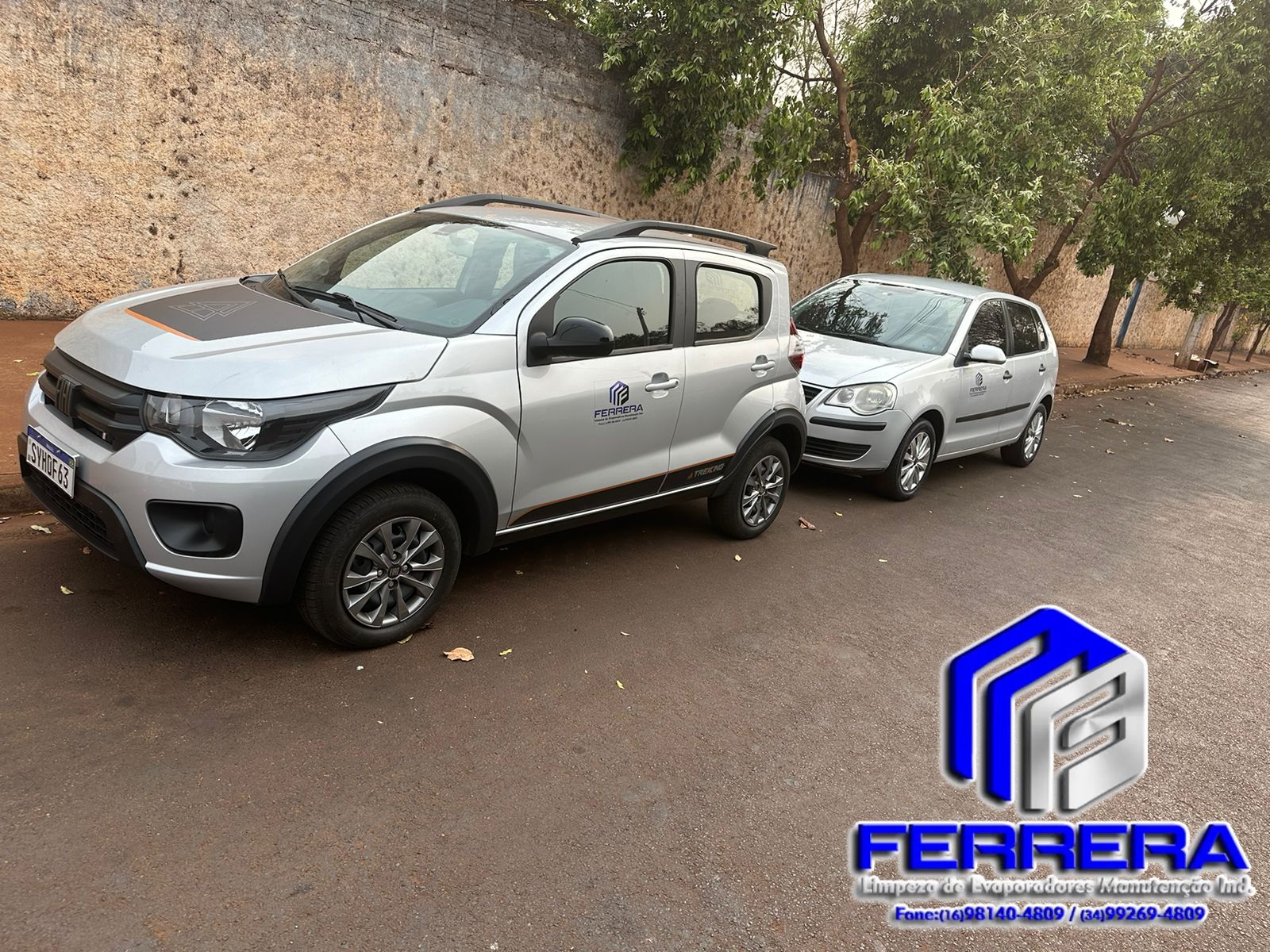 Veículos prata e cinza da frota para limpeza e manutenção de evaporadores, alinhados em uma área urbana com árvores e um muro ao fundo.