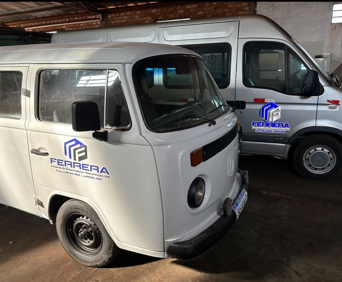 Kombi branca e van prata estacionados em uma garagem interna, usados como parte da frota de serviços industriais da empresa.