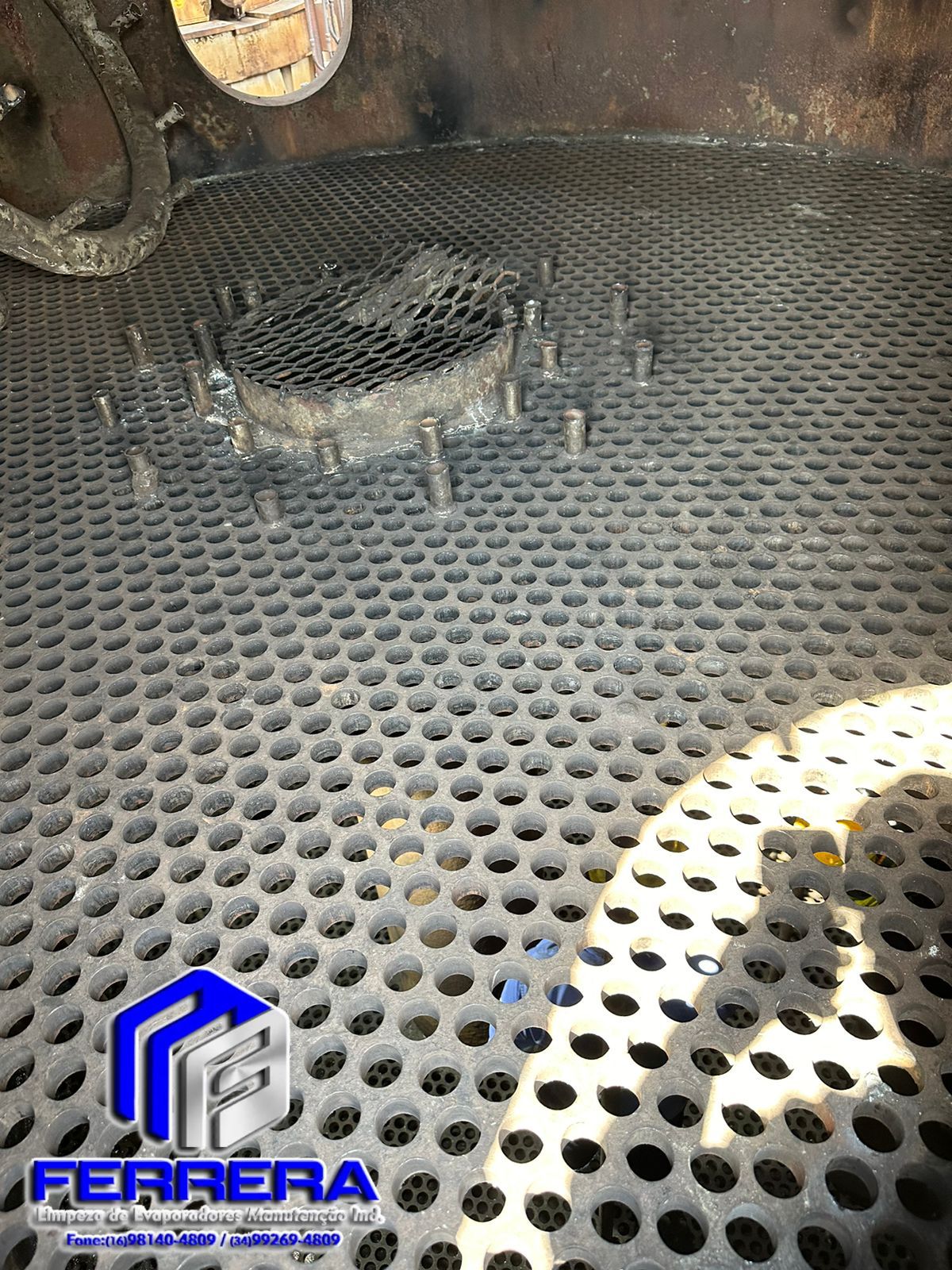 Piso metálico perfurado e sujo, com peças de manutenção de equipamento industrial.