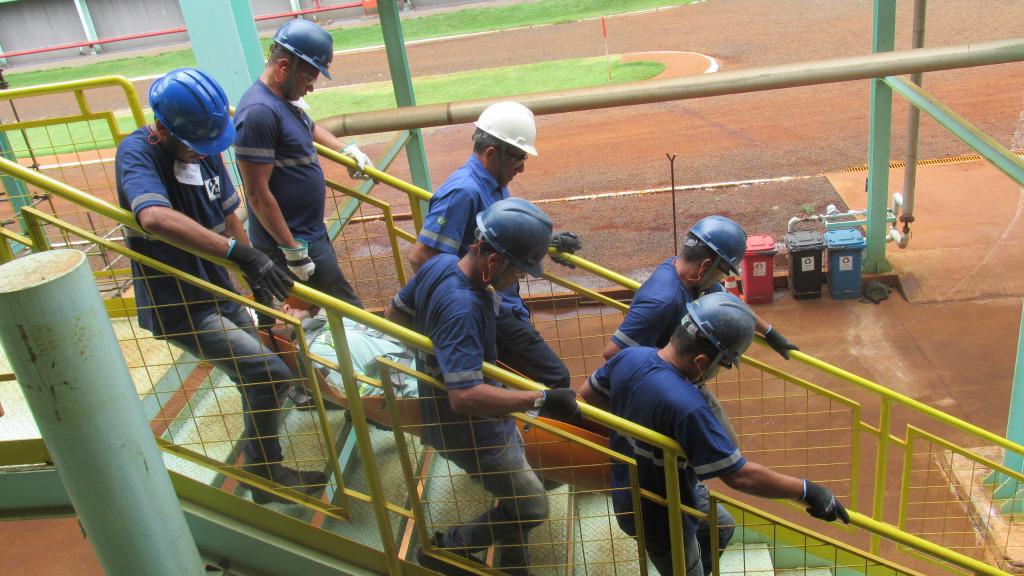 Equipe de manutenção industrial em uniforme azul e capacete, descendo escadaria de uma fábrica.