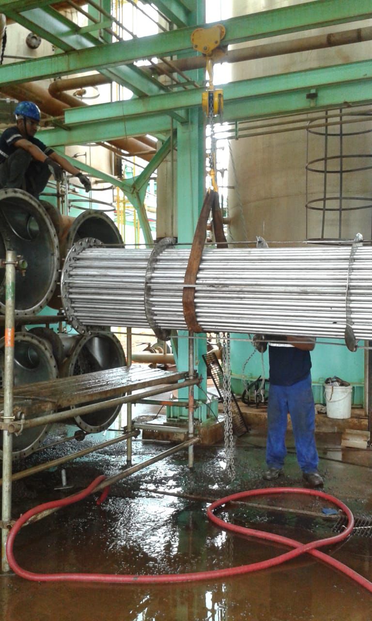Profissionais de limpeza e manutenção industrial içando um feixe tubular de evaporador com talha.