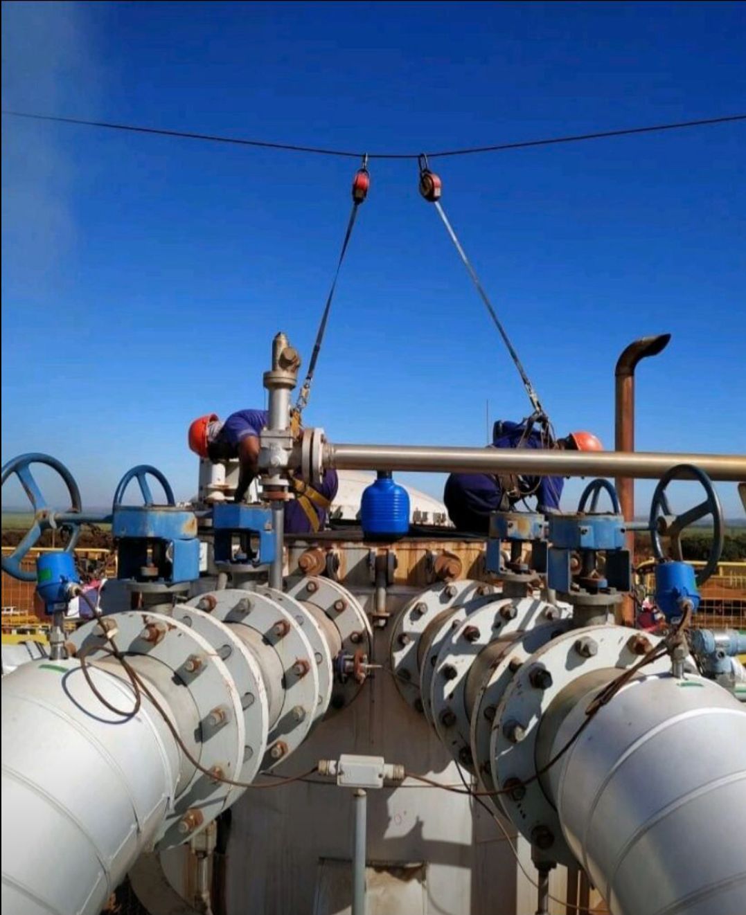 Manutenção externa em altura: dois técnicos da Ferrera em cima de um sistema de tubulações e válvulas industriais.